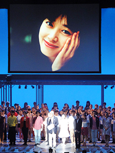 故夏目雅子さんの遺影の下で挨拶する「夏目雅子ひまわり基金」の小達代表事務局長